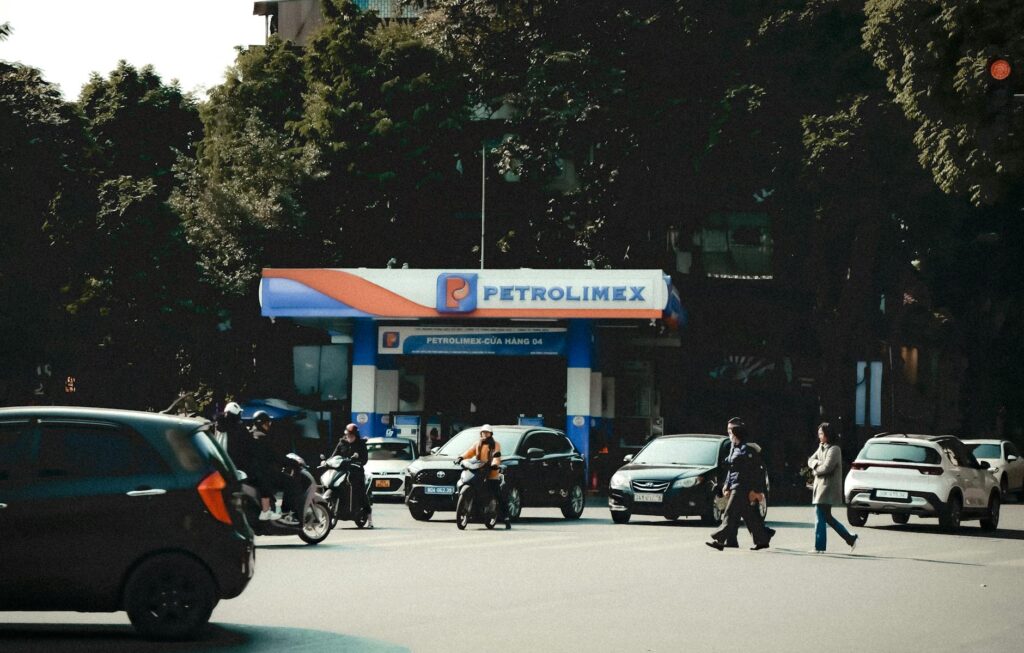 Busy street scene with vehicles and pedestrians at a Petrolimex gas station under daylight.